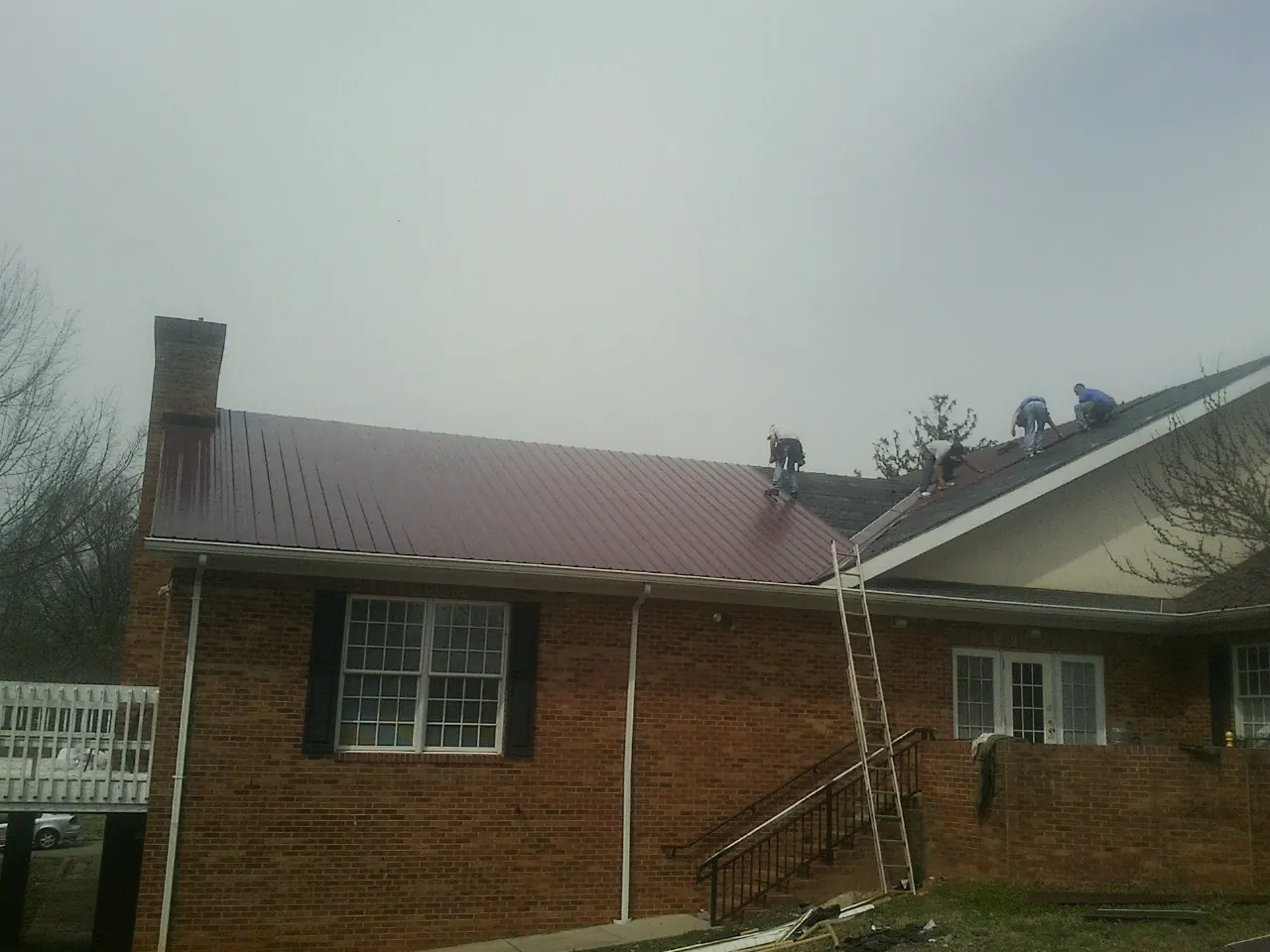 Crew setting red metal roofing panels on a brick home in Adamsville
